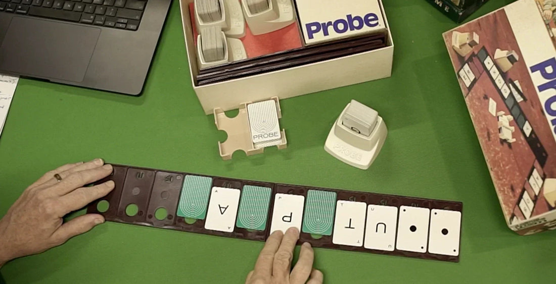 Probe card game laid out on a tabletop showing the open box and a series of playing cards with letters that form a word