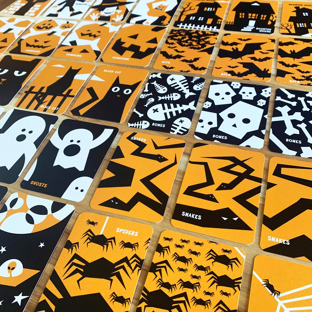A close-up of Gard game featuring Halloween-themed illustrations of ghosts, spiders, skeletons, bats, and haunted houses arranged in a grid on a wooden surface.